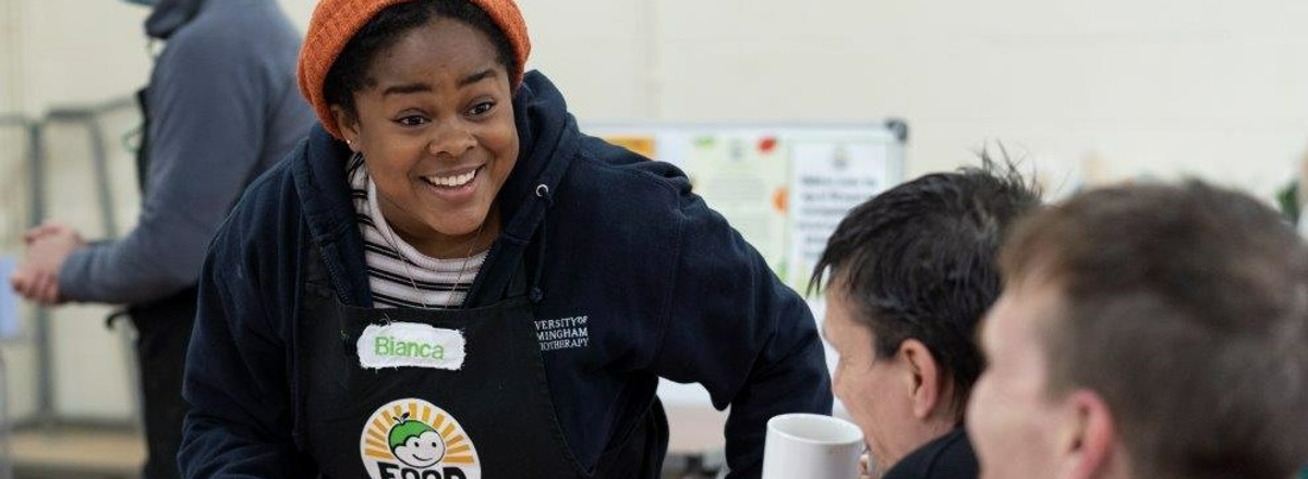 Header image showing a FoodCycle volunteer chatting to benificaries of the charity