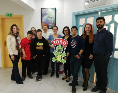 Beneficaries and members of the Türkiye Down Syndrom Association standing for a photo with the charity logo