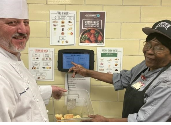 Two Compass chefs in kitchen using Waste Not 2.0 food waste tracking system