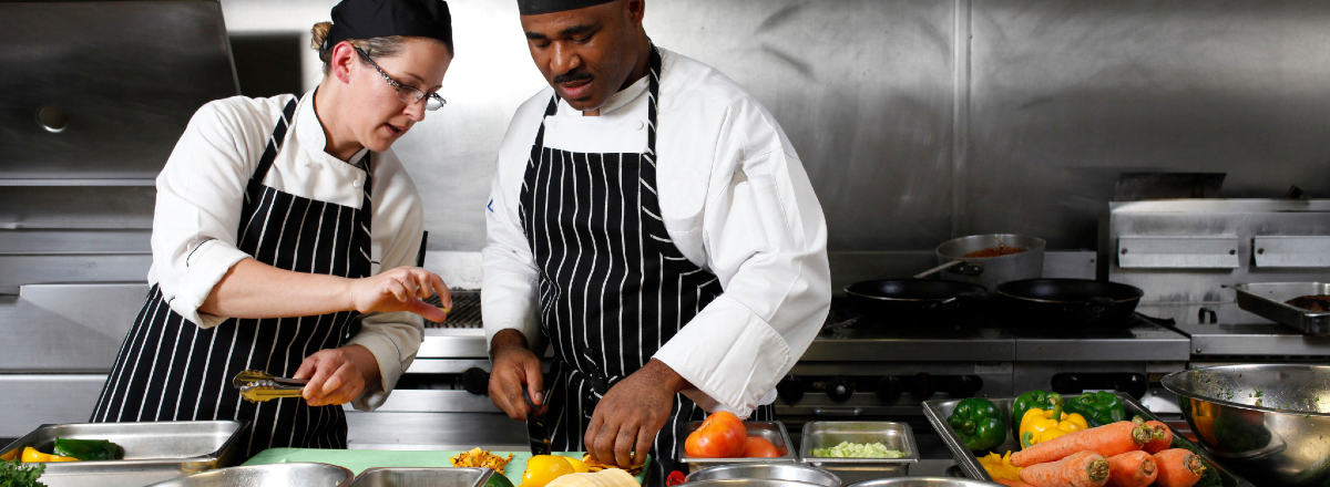 Two chefs talking whilst preparing food in kitchen